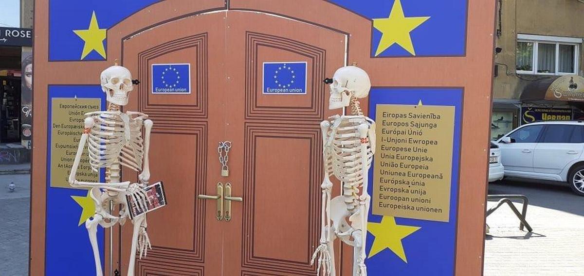 Skopje (Macedonia del Nord), 3 maggio 2022. Due scheletri di plastica in attesa davanti a un cartonato che raffigura le porte dell'Ue