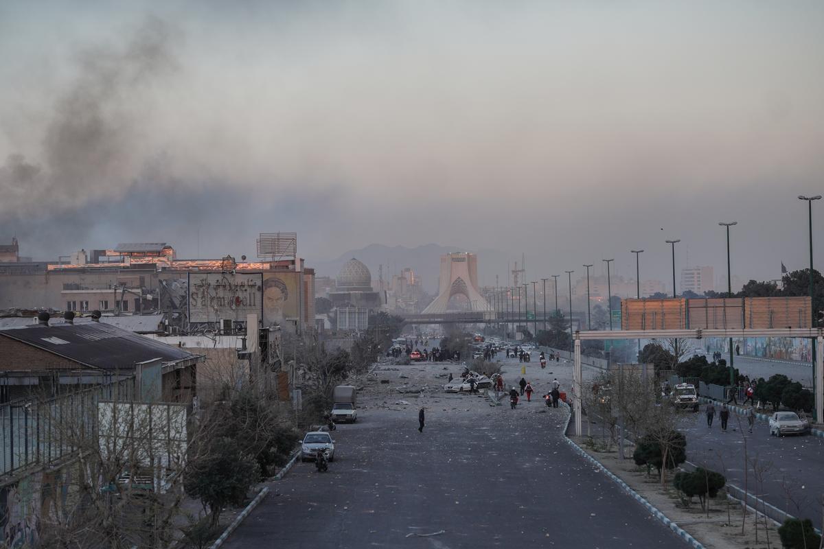 Teheran, i danni causati dai bombardamenti su una strada della capitale iraniana. Sullo sfondo, la torre Azadi, simbolo della città, avvolta nel fumo 