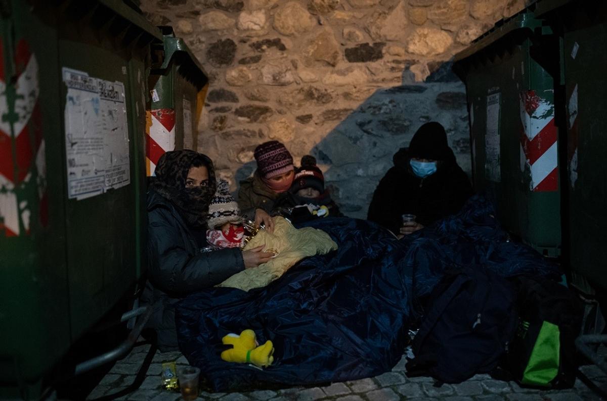 Una famiglia afghana si ripara dal freddo tra i bidoni della spazzatura prima di partire verso il confine italo-francese. Foto di Valerio Muscella e Michele Lapini