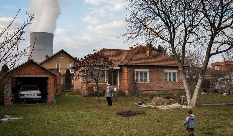 Una donna di Obiliq assieme al nipote nella parte vecchia della cittadina. Dopo la morte del marito la famiglia ha deciso di trasferirsi a Pristina e solo occasionalmente frequenta la casa. È morto a 61 anni a causa di un cancro che lo ha portato via nell'arco di tredici mesi. "È strano, non capivamo perché – dice la figlia era un uomo in forma, cintura nera di judo. Credo gli sia venuto per lo stress del lavoro". Nel vicinato diverse persone sono decedute o soffrono di tumori, metà delle case sono abbandonate.