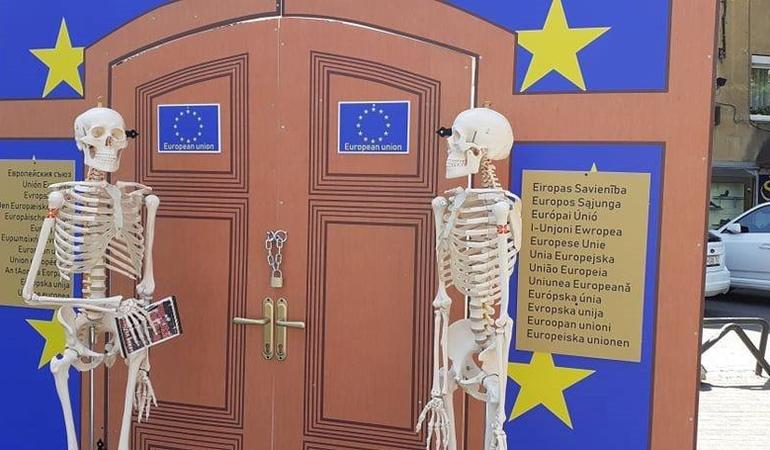 Skopje (Macedonia del Nord), 3 maggio 2022. Due scheletri di plastica in attesa davanti a un cartonato che raffigura le porte dell'Ue