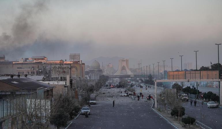 Teheran, i danni causati dai bombardamenti su una strada della capitale iraniana. Sullo sfondo, la torre Azadi, simbolo della città, avvolta nel fumo 
