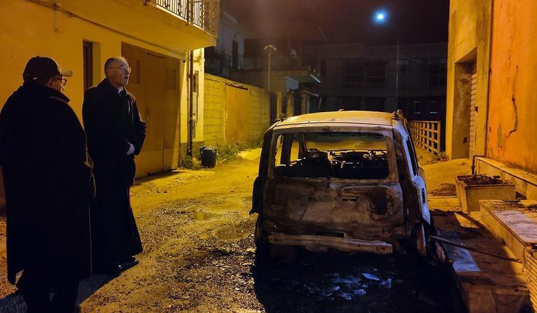 Da sinistra, don Gianni Rigoli e il vescovo di Oppido Mamertina Palmi, Giuseppe Alberti, vicino all'auto del parroco data alle fiamme (Foto Diocesi Oppido-Palmi)