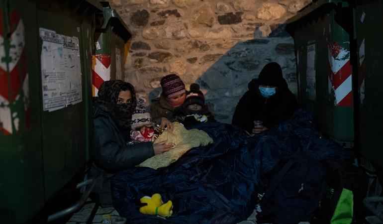 Una famiglia afghana si ripara dal freddo tra i bidoni della spazzatura prima di partire verso il confine italo-francese. Foto di Valerio Muscella e Michele Lapini