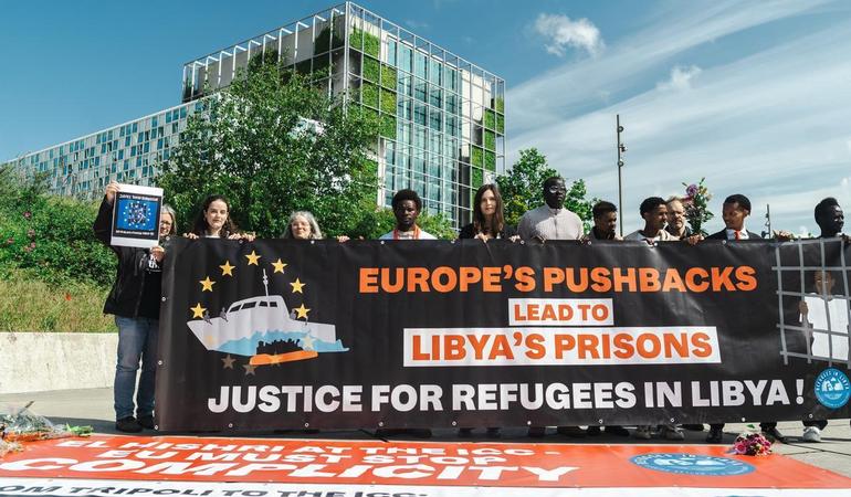 L'Aia (Paesi Bassi), 21 maggio 2026. Attiviste e attivisti espongono uno striscione che denuncia la complicità dell'Europa nei crimini nei centri di detenzione in Libia. Il sesto da sinistra è Lam Magok. Foto di Refugees in Libya