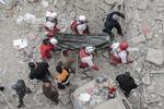 I soccorritori portano una barella con un corpo. Tra le macerie sono visibili degli orsetti peluche